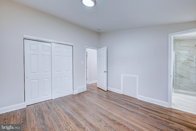 unfurnished bedroom with wood finished floors, a closet, baseboards, and connected bathroom