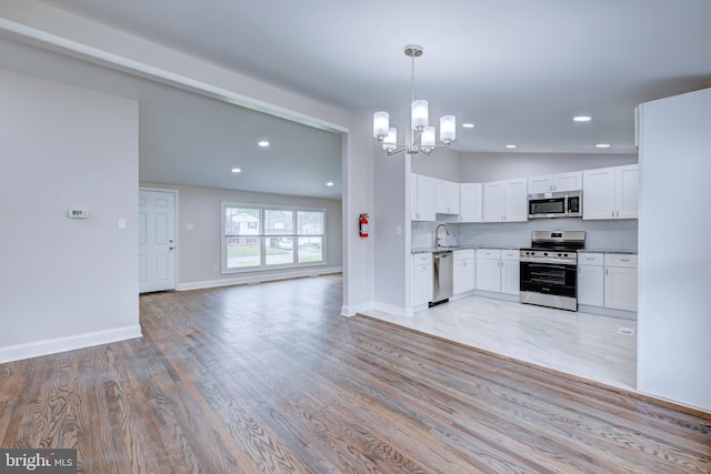 kitchen featuring appliances with stainless steel finishes, a chandelier, light wood-style floors, open floor plan, and white cabinetry