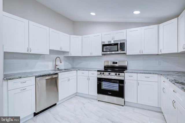 kitchen with stainless steel appliances, a sink, vaulted ceiling, light marble finish floors, and light stone counters