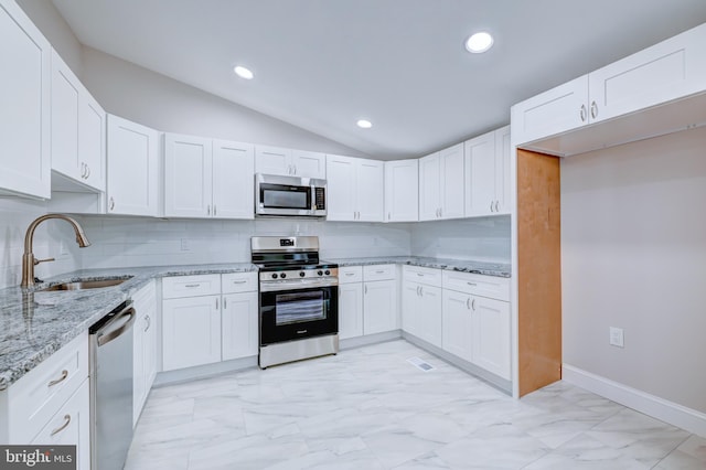 kitchen featuring stainless steel appliances, a sink, lofted ceiling, light marble finish floors, and light stone countertops