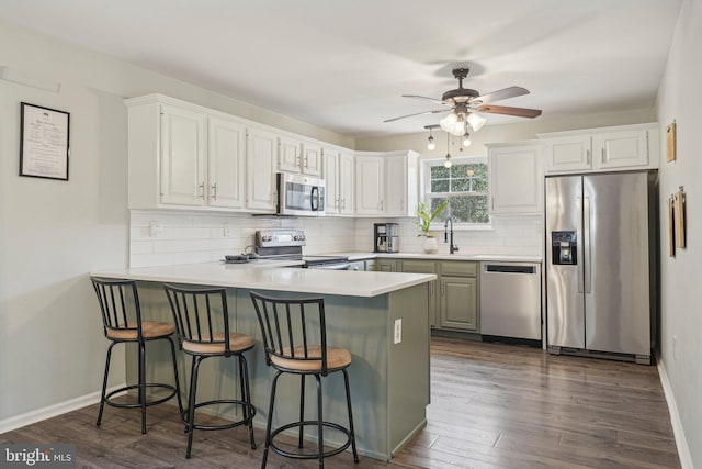 kitchen featuring appliances with stainless steel finishes, a peninsula, a sink, backsplash, and ceiling fan