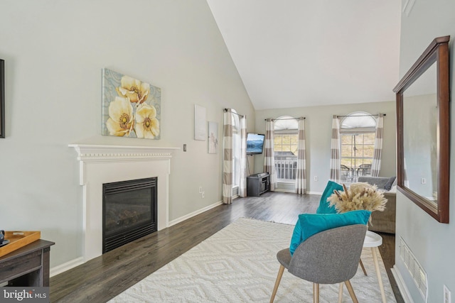 living room featuring wood finished floors, high vaulted ceiling, a glass covered fireplace, and baseboards