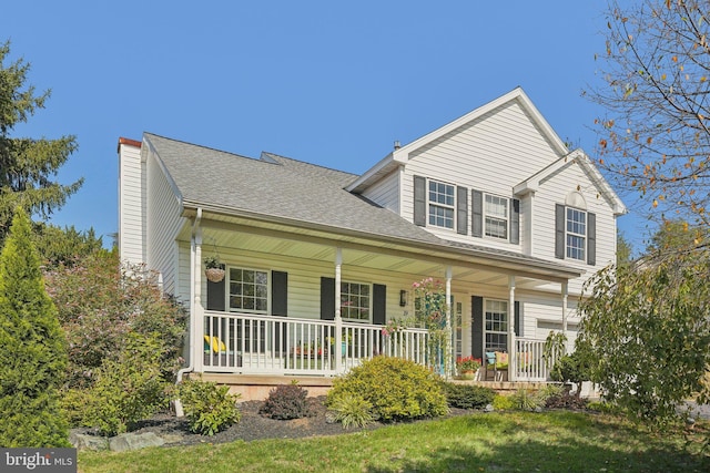 traditional-style home featuring a porch, a chimney, and roof with shingles