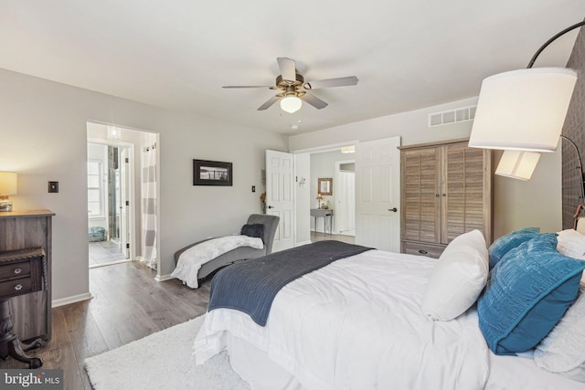 bedroom featuring wood finished floors, baseboards, ceiling fan, and ensuite bath