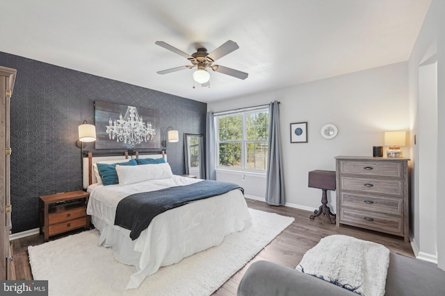 bedroom with baseboards, wallpapered walls, wood finished floors, an accent wall, and a ceiling fan