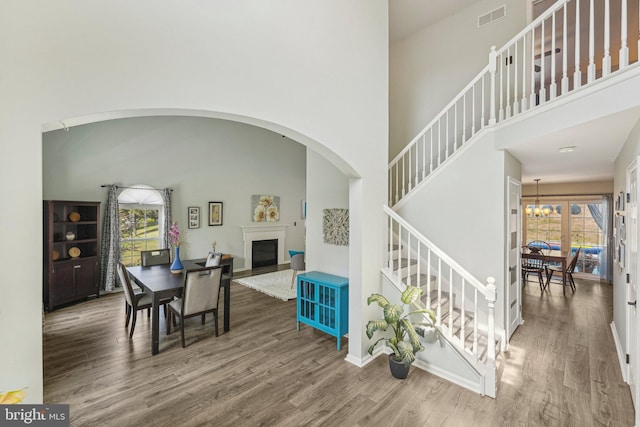 dining space featuring healthy amount of natural light, wood finished floors, stairway, a towering ceiling, and a fireplace