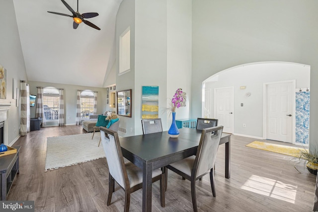 dining room featuring high vaulted ceiling, ceiling fan, arched walkways, wood finished floors, and baseboards