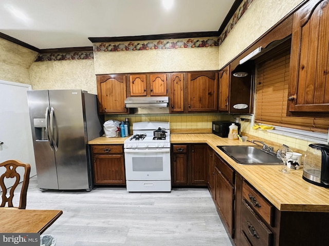 kitchen featuring stainless steel fridge, white gas stove, a sink, under cabinet range hood, and ornamental molding