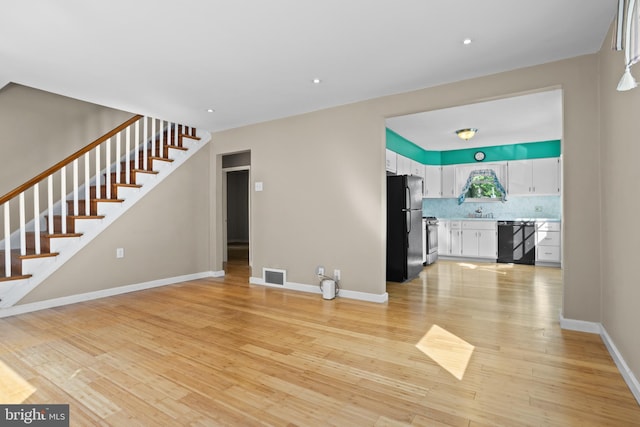 unfurnished living room featuring light wood-style flooring, stairway, baseboards, and recessed lighting