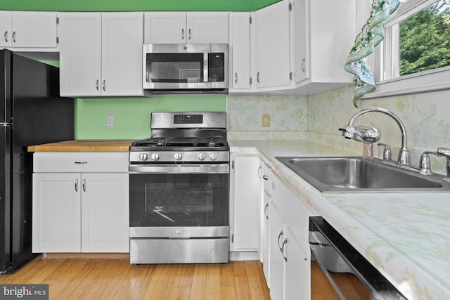 kitchen with appliances with stainless steel finishes, a sink, light countertops, and white cabinets