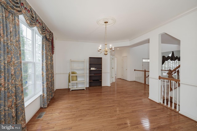 unfurnished dining area featuring a chandelier, light wood-style flooring, and crown molding