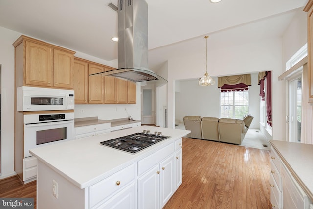 kitchen with white appliances, island range hood, light countertops, light wood-style floors, and a chandelier