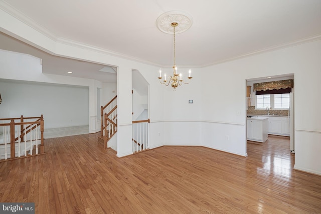 unfurnished dining area with a chandelier, light wood-style flooring, ornamental molding, and a sink