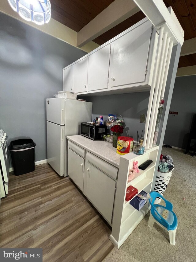kitchen with light countertops, white cabinets, beam ceiling, freestanding refrigerator, and wood finished floors