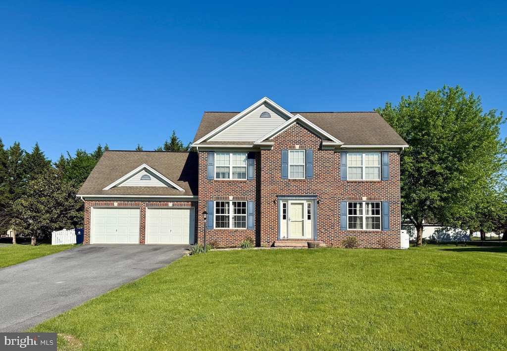 colonial inspired home featuring asphalt driveway, an attached garage, brick siding, and a front lawn