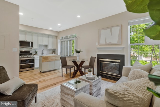 living area featuring light wood-style floors, a glass covered fireplace, and recessed lighting