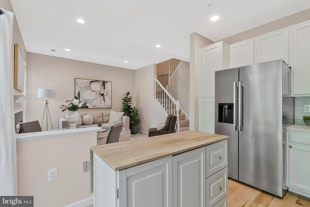 kitchen with stainless steel refrigerator with ice dispenser, light wood-style floors, a kitchen island, open floor plan, and recessed lighting