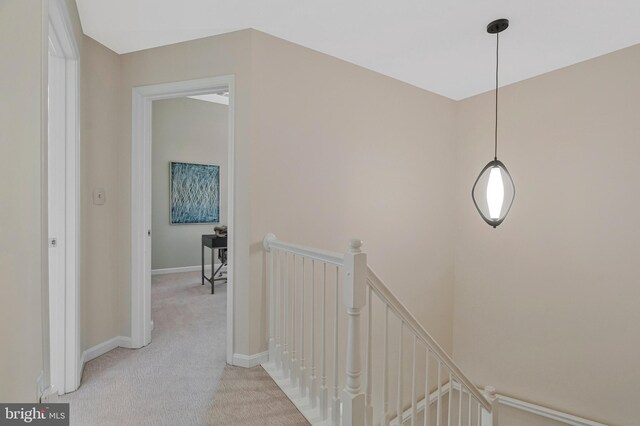 hall with an upstairs landing, light colored carpet, and baseboards