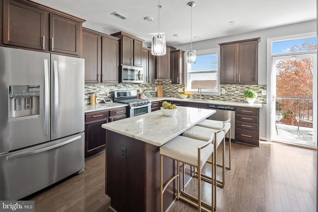 kitchen with appliances with stainless steel finishes, a sink, dark brown cabinetry, a kitchen bar, and plenty of natural light