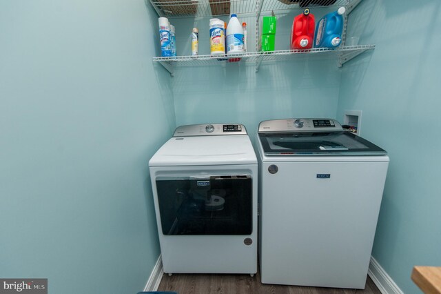 clothes washing area featuring washer and clothes dryer, wood finished floors, and baseboards