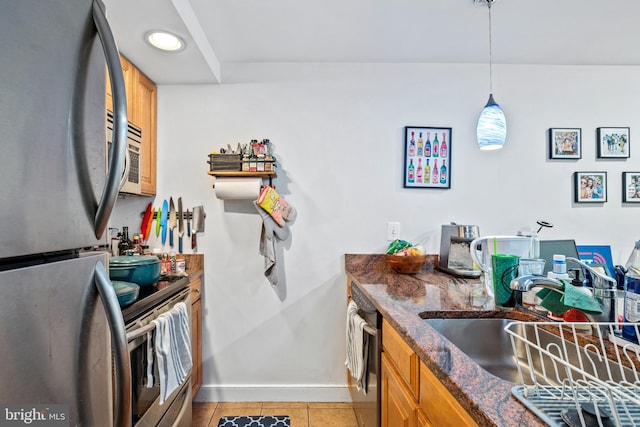 kitchen with stainless steel appliances, a sink, baseboards, light tile patterned floors, and brown cabinetry