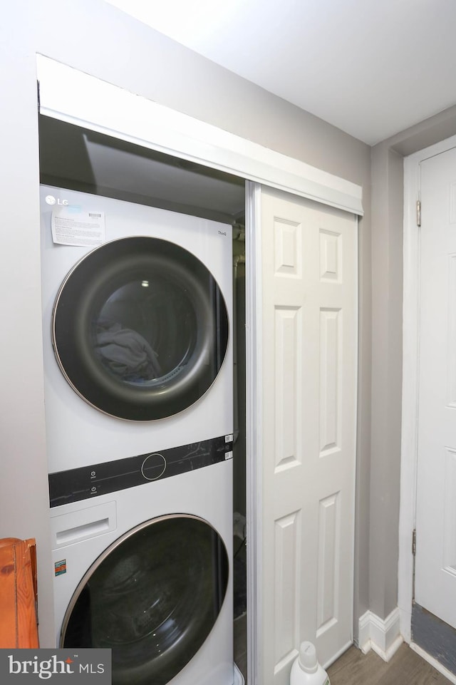 washroom with stacked washer / dryer, wood finished floors, and baseboards