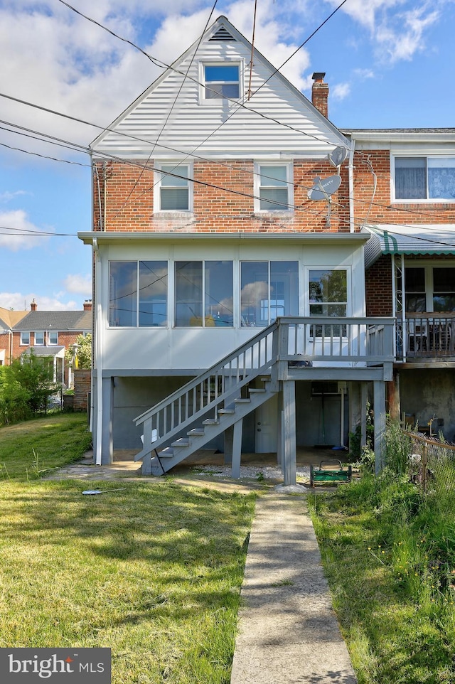 rear view of property featuring a lawn, brick siding, a chimney, a deck, and stairway
