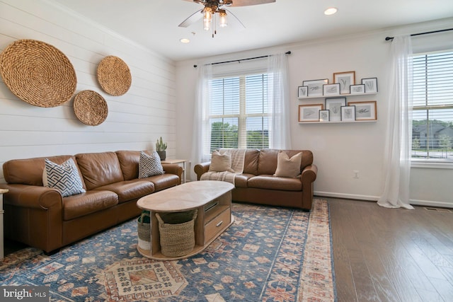 living area featuring ceiling fan, baseboards, wood-type flooring, wooden walls, and crown molding