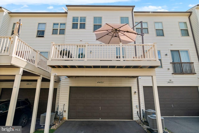 back of property with a garage, a balcony, driveway, and central AC