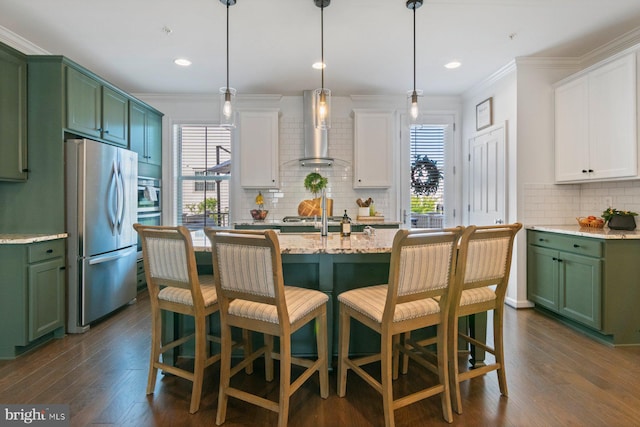kitchen with wall chimney range hood, freestanding refrigerator, tasteful backsplash, green cabinets, and plenty of natural light