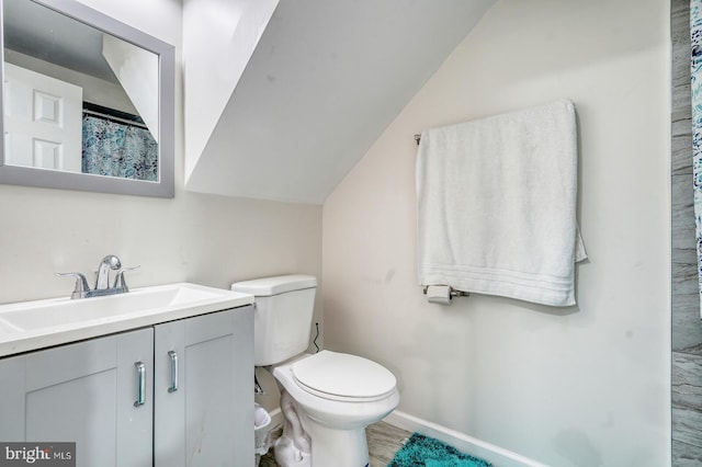 bathroom with toilet, vanity, baseboards, and vaulted ceiling