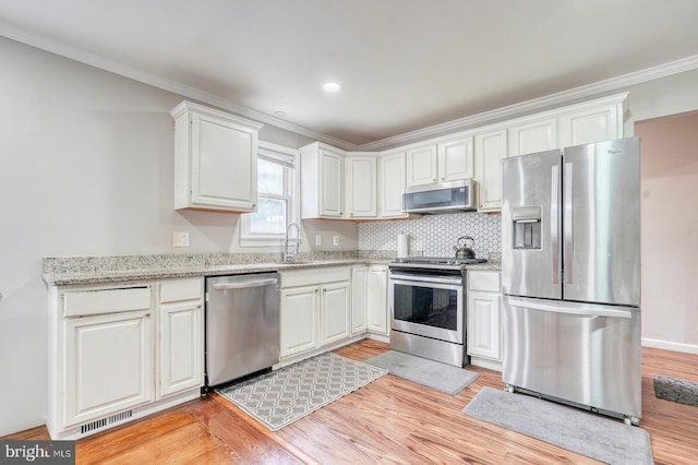 kitchen featuring stainless steel appliances, ornamental molding, light wood-type flooring, white cabinetry, and light stone counters