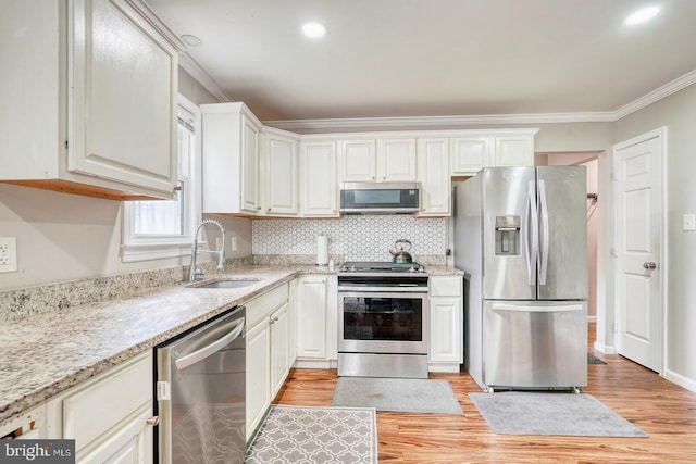 kitchen with stainless steel appliances, a sink, crown molding, light wood-style flooring, and tasteful backsplash