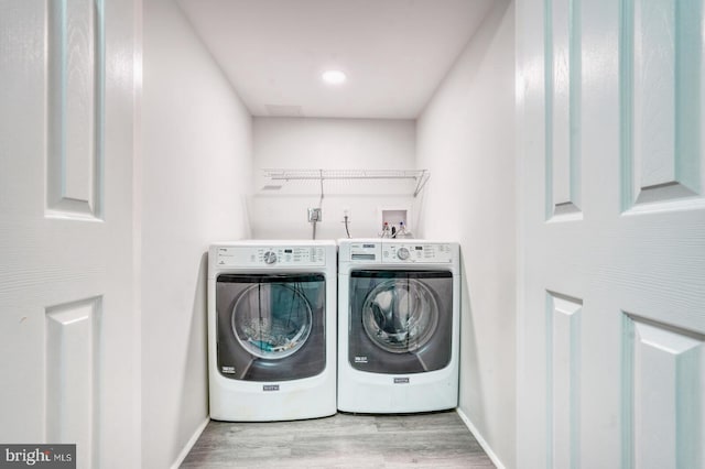 clothes washing area with washing machine and dryer, wood finished floors, and baseboards