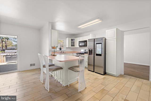 316 Nautilus Dr, Manahawkin, NJ 08050 - kitchen with stainless steel appliances, glass insert cabinets, a peninsula, light wood finished floors, and white cabinetry