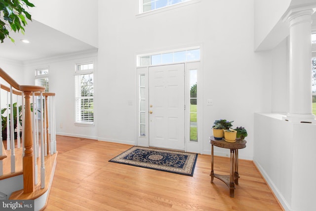 entrance foyer with ornate columns, wood finished floors, baseboards, ornamental molding, and stairs