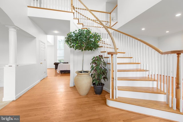 staircase with wood finished floors, a high ceiling, recessed lighting, baseboards, and ornate columns