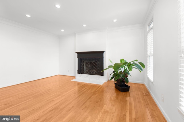 unfurnished living room with light wood-type flooring, ornamental molding, recessed lighting, a fireplace with flush hearth, and baseboards