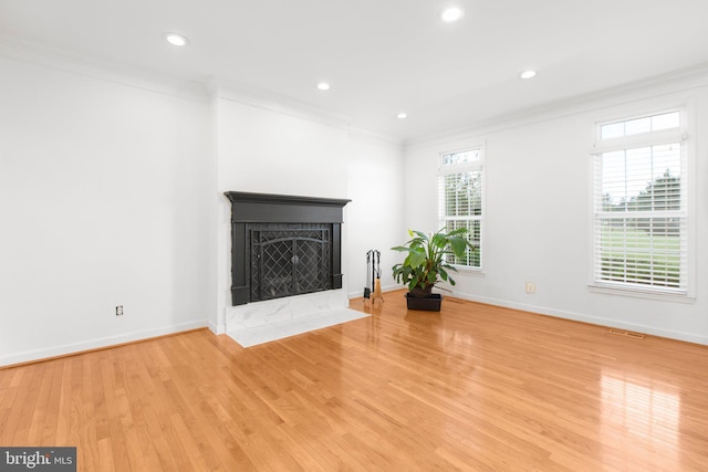 unfurnished living room featuring ornamental molding, light wood finished floors, baseboards, a fireplace with flush hearth, and recessed lighting