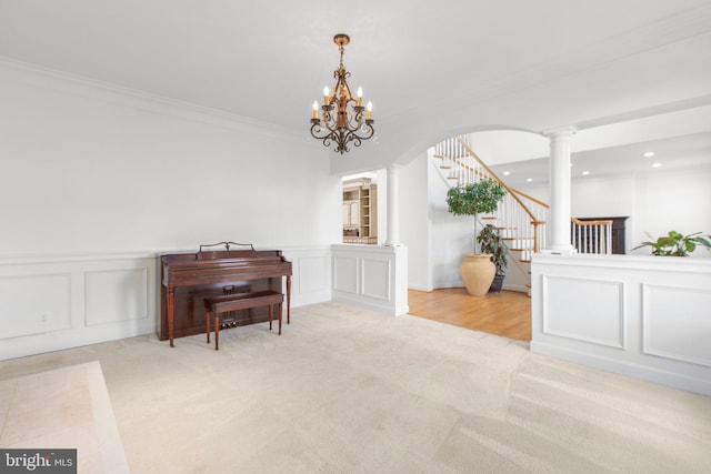 sitting room with light carpet, ornamental molding, a decorative wall, ornate columns, and stairway