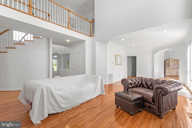 living room with arched walkways, ornamental molding, wood finished floors, stairway, and baseboards