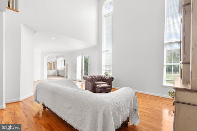 bedroom featuring arched walkways, multiple windows, wood finished floors, a towering ceiling, and recessed lighting