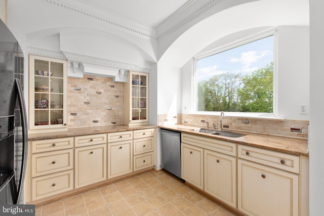 kitchen with cream cabinetry, dishwasher, black fridge, a sink, and tasteful backsplash