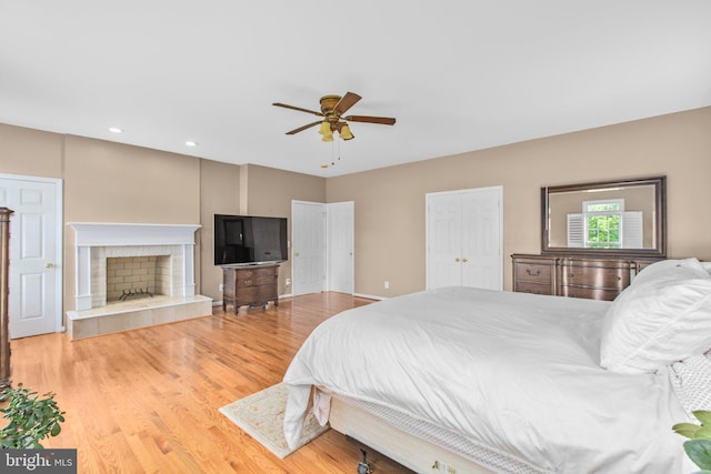 bedroom with light wood-type flooring, recessed lighting, a tiled fireplace, and a ceiling fan