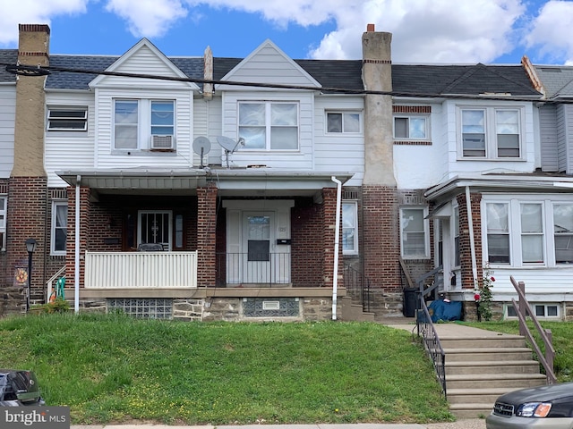 view of property with a chimney, covered porch, a front yard, brick siding, and cooling unit