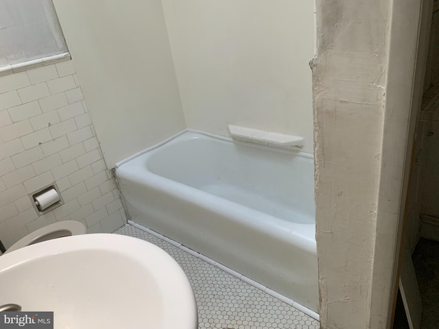 full bath with a tub to relax in, a sink, and tile walls