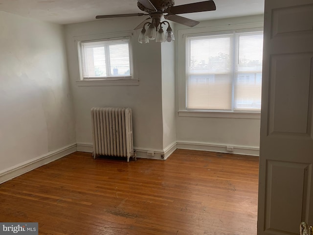 unfurnished room featuring radiator, a ceiling fan, hardwood / wood-style flooring, and baseboards
