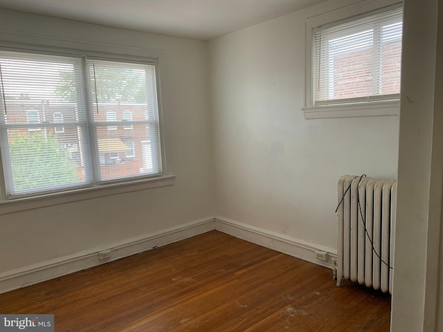 empty room with radiator, dark wood-type flooring, and healthy amount of natural light