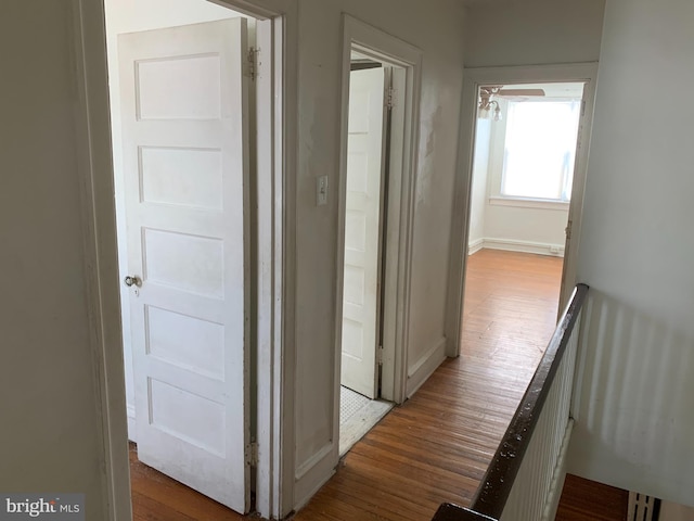 corridor featuring wood finished floors, an upstairs landing, and baseboards