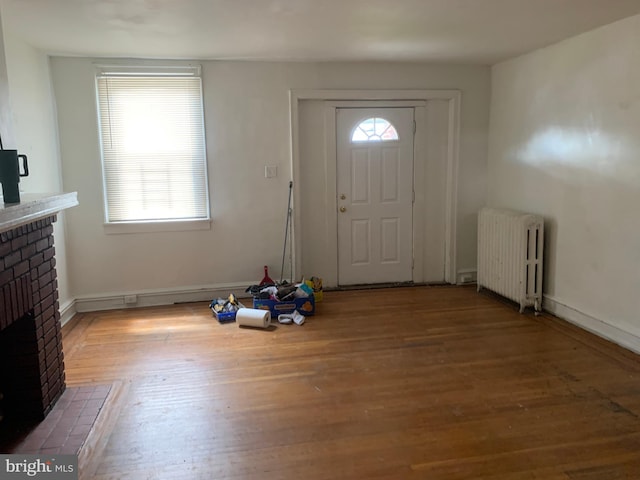foyer featuring radiator, a brick fireplace, wood finished floors, and baseboards